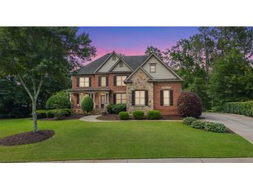 Charming two-story brick home with stone accents, well-manicured lawn, and mature trees during sunset at 5925 Water Mark Dr, Cumming, GA 30040