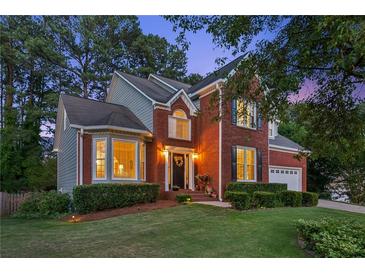 Charming brick home featuring manicured lawn, mature trees and inviting front entrance at twilight at 440 Laurian Nw Way, Kennesaw, GA 30144