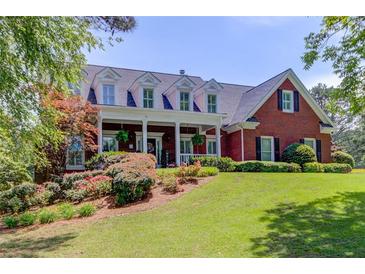 Charming two-story brick home with a manicured lawn, lush landscaping, and inviting covered front porch at 1292 Green Turf Dr, Snellville, GA 30078
