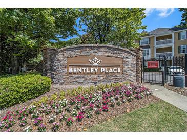 Stone sign for Bentley Place with colorful flowers and a glimpse of the buildings behind the gated entrance at 328 Bentley Pl # 328, Tucker, GA 30084