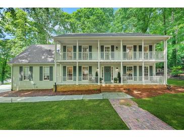 Charming two-story home featuring double balconies, a brick foundation, and lush landscaping at 3870 Windhurst Dr, Lilburn, GA 30047