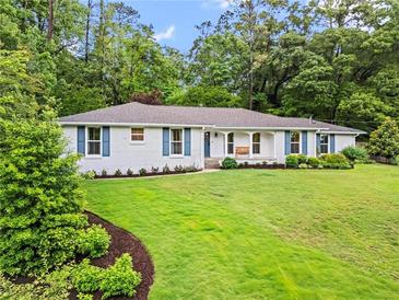Charming one-story home with white brick, blue shutters, and a lush green lawn surrounded by mature trees at 4855 Kendall Ct, Atlanta, GA 30342