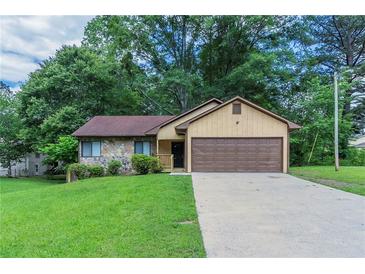 Charming single-story home with a stone accent wall, a brown garage door, and a lush green lawn at 8350 Gledstone Way, Fairburn, GA 30213