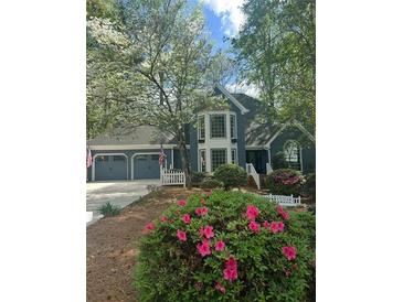 Charming two-story home with a three-car garage, landscaped yard, and blooming pink azaleas under a canopy of trees at 3017 Lana Ln, Marietta, GA 30066