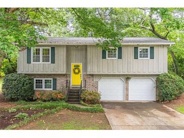 Charming home features a bright yellow door, a two-car garage, and lovely landscaping at 4171 Whispering Forest Sw Ct, Lilburn, GA 30047