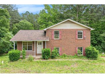Charming two-story brick home featuring a covered front porch and red shutters surrounded by lush greenery at 1576 King Mill Rd, Mcdonough, GA 30252