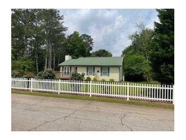 Charming single-story home with a green roof and a white picket fence bordering a manicured front yard at 173 Elder Dr, Social Circle, GA 30025
