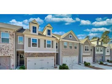 Attractive townhome exterior with a well-maintained lawn and attached garages underneath a partly cloudy, blue sky at 2711 Kemp Ct, Conyers, GA 30094