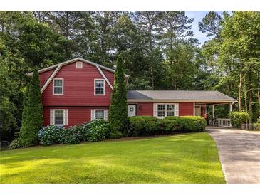 Charming red two-story home with a well-manicured lawn, lush landscaping, and a driveway leading to the carport at 1102 Waverly Dr, Lawrenceville, GA 30046