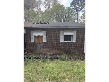 Image of the exterior brick wall, roof damage, with overgrown lawn and boarded window at 2625 Baker Nw Rd, Atlanta, GA 30318