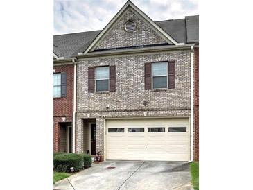 Two-story townhome featuring a one-car garage, brick facade, and well-maintained landscaping at 7177 Fringe Flower Dr, Austell, GA 30168