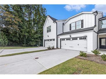 A view of a modern white townhouse with attached garage, complemented by a concrete driveway and manicured landscaping at 1704 Hyssop Se Blvd, Smyrna, GA 30126