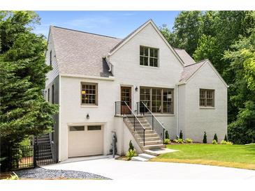 Charming white brick home featuring a well-manicured lawn, attached garage, and inviting staircase leading to the front door at 1327 Harvard Ne Rd, Atlanta, GA 30306