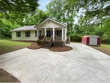 Charming home with front porch and a concrete driveway surrounded by green trees and a storage shed in the back at 355 Marietta Hwy, Roswell, GA 30075