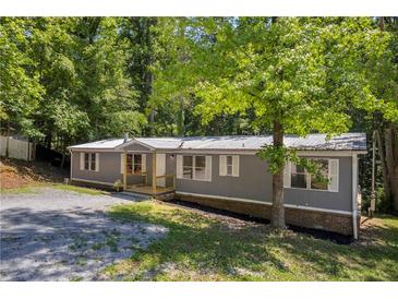 Charming gray home with a metal roof, complemented by lush, mature trees and a gravel driveway at 6235 Akins Way, Cumming, GA 30041