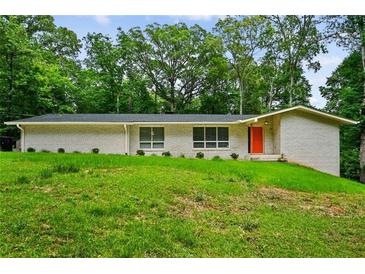 Charming single-story white brick home with a well-manicured green lawn and an orange front door at 3332 Saint John Dr, East Point, GA 30344
