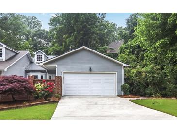 Attached two-car garage with a concrete driveway and gray siding surrounded by beautiful landscaping at 2983 Crosswycke Forest Dr, Brookhaven, GA 30319