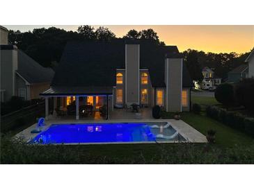 Backyard view of the house with an illuminated blue inground pool and covered patio at dusk at 5440 Old Haven Ct, Cumming, GA 30041