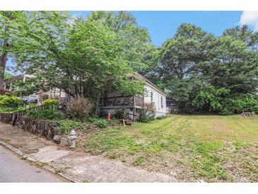 Quaint white home with a welcoming front porch, surrounded by mature trees and a green lawn at 1052 Curran Nw St, Atlanta, GA 30318
