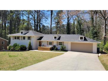 Charming white brick home featuring a long driveway, attached garage and manicured front yard and wooded backdrop at 1978 Fisher Ne Trl, Atlanta, GA 30345