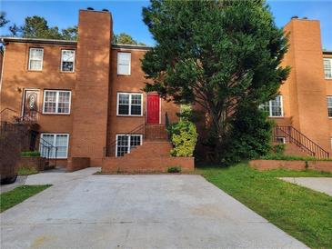 Brick townhome showcasing a red front door and staircase access with a concrete driveway and mature trees at 115 Davis Mill Ct, Lawrenceville, GA 30044