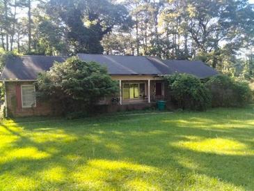 Lawn view of the home, a single-story house with an overgrown yard and mature trees at 1627 Norden Rd, Riverdale, GA 30296