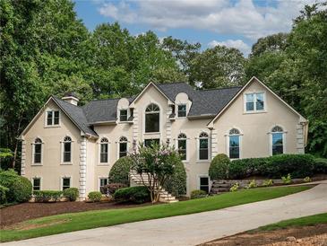 Stunning two-story home featuring lush landscaping and arched windows, set against a backdrop of mature trees at 5940 Plantation Dr, Roswell, GA 30075