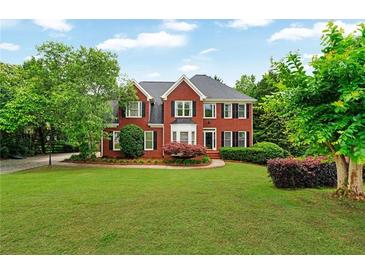 Charming two-story red brick home with a lush green lawn, complemented by mature trees and manicured landscaping at 209 Breckenridge Ct, Canton, GA 30115