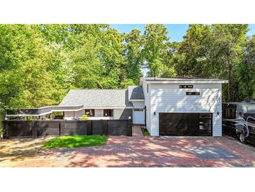 Contemporary home featuring a two-car garage, black privacy fence, brick driveway and mature landscaping at 1048 Indian Hills Pkwy, Marietta, GA 30068