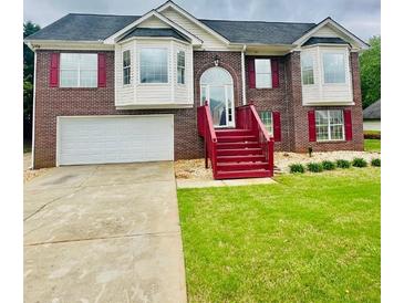 Traditional brick home features a two-car garage, manicured lawn, and red accents around the windows and front steps at 80 Fields Creek Way, Covington, GA 30016