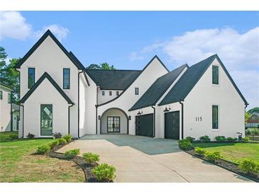 Stunning exterior of a modern home with black trim, arched doorway, and a concrete driveway leading to a two-car garage at 115 Thome Dr, Alpharetta, GA 30022