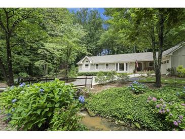 Inviting home exterior featuring stone facade, mature landscaping, and charming wooden bridge at 7265 Hunters Branch Dr, Sandy Springs, GA 30328