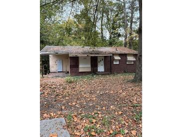 An exterior shot of a house with boarded up windows, a yard full of leaves, and a roof in need of repair at 711 Alfred Nw Rd, Atlanta, GA 30331