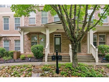 Inviting brick townhouse with a covered porch, complemented by lush landscaping and a charming tree at 4358 Grove Field Ct, Suwanee, GA 30024