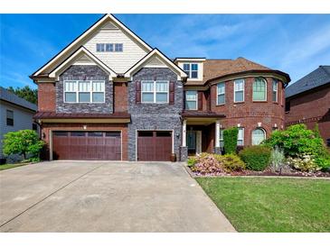 Elegant brick and stone home featuring a three-car garage, manicured lawn, and beautiful landscaping at 3642 Lake Estates Way Way, Atlanta, GA 30349