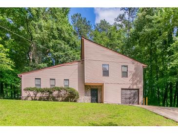 Charming home featuring a manicured lawn, tall trees, a garage, and a unique architectural design at 3851 Natalie Way, Ellenwood, GA 30294