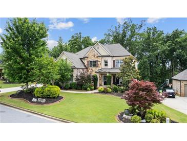Charming brick home featuring manicured lawn, stone accents, and mature trees on a sunny day at 1980 Marcia Overlook Dr, Cumming, GA 30041