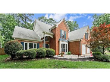 Charming two-story brick home featuring a well-manicured lawn, lush shrubbery, and an attached two-car garage at 1340 Gran Forest Dr, Cumming, GA 30041