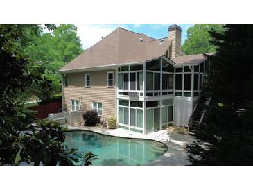 Backyard view of a home's screened porch and refreshing pool surrounded by lush greenery at 115 Windover Ct, Roswell, GA 30075