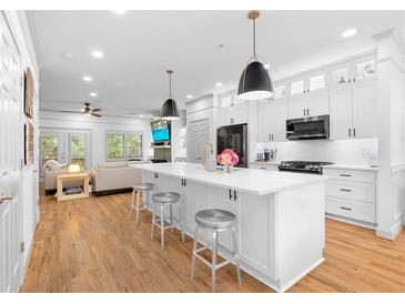 Bright kitchen with white cabinetry, stainless steel appliances, and hardwood floors open to a living room at 208 Wade Creek Rd, Alpharetta, GA 30009