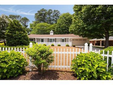 Charming single-story home featuring a white picket fence and mature landscaping at 1100 Tuxedo Dr, Roswell, GA 30075
