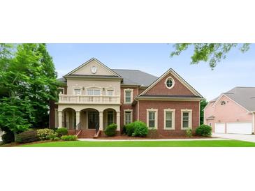Elegant brick home featuring a covered porch with columns, a balcony, manicured lawn, and lush landscaping at 1565 Briergate Dr, Duluth, GA 30097