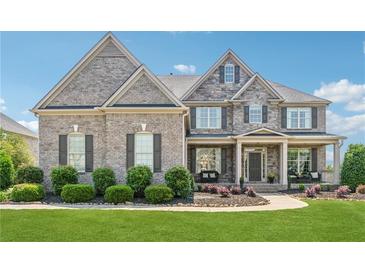 Beautiful two-story brick home with a manicured lawn, flower beds, and a covered front porch with seating at 5070 Laurel Ridge Dr, Cumming, GA 30040