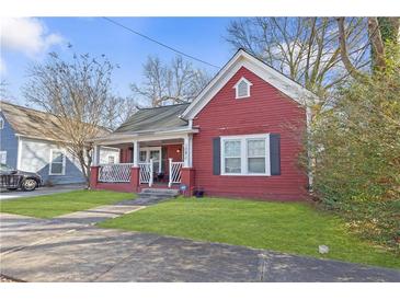 Charming red home featuring a cozy front porch, complemented by green grass and mature trees at 1081 Longley Nw Ave, Atlanta, GA 30318