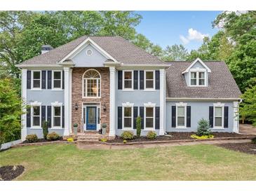 Charming two-story home with blue exterior, manicured lawn, mature trees, and traditional architectural details at 1039 Avery Creek Dr, Woodstock, GA 30188