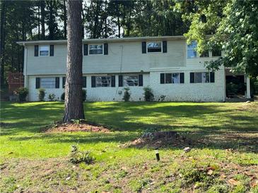 Two-story home with light siding, black shutters and a green lawn surrounded by tall trees at 2510 Lakeshore Ne Dr, Conyers, GA 30012