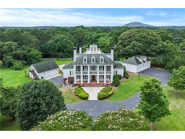Expansive white home featuring a green roof, black chimneys and shutters, manicured landscaping and a circular driveway at 2595 Ross Rd, Snellville, GA 30039