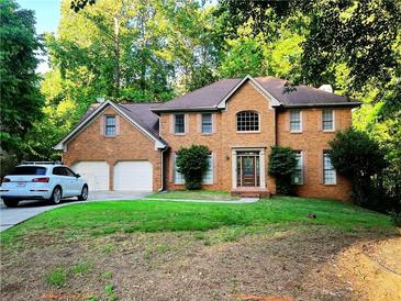 Charming brick home featuring an attached two-car garage, lush lawn, and mature trees at 11575 Wildwood Springs Dr, Roswell, GA 30075