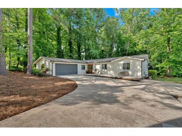 Charming single-story home featuring a gray garage, driveway, wooden door, and lush, mature trees surrounding the property at 4492 Riverwood Cir, Decatur, GA 30035