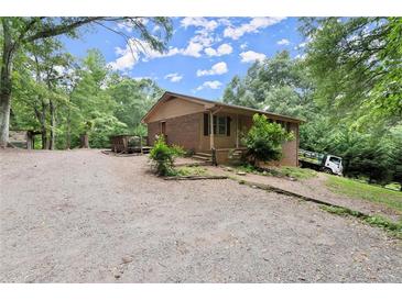Charming brick home with a covered porch and a spacious gravel driveway, surrounded by lush greenery at 129 Bill Smith Dr, Canton, GA 30114